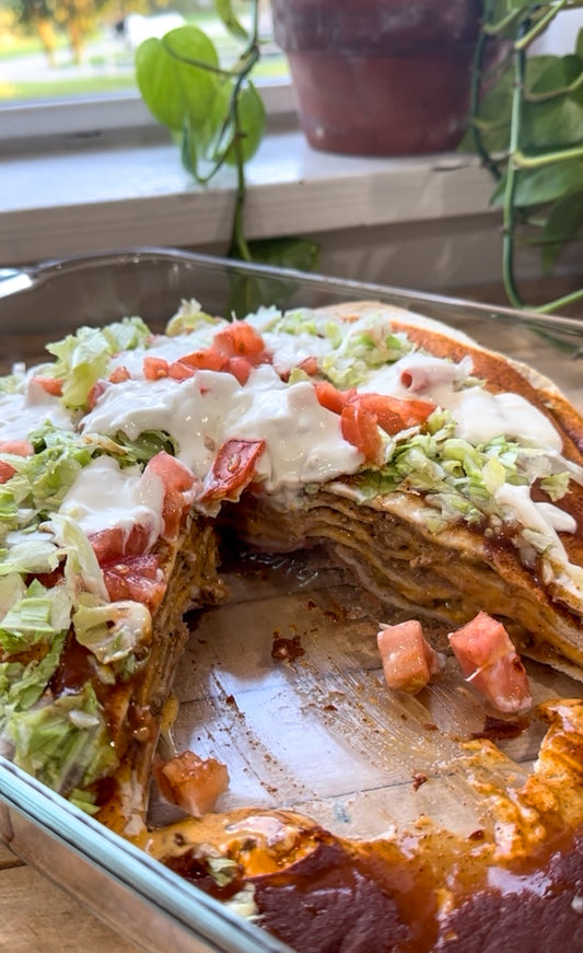 Close-up of layered taco casserole with tortillas, taco meat, queso, refried beans, lettuce, tomato, and sour cream in a glass baking dish